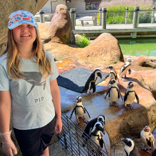 Smiling girl stands in habitat, in front of penguins
