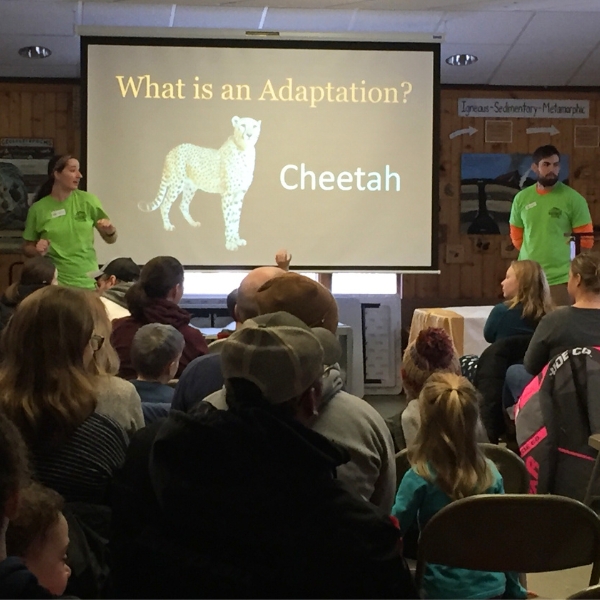 Zoo teachers stand in front of audience, with screen that reads "what is an adaptation"