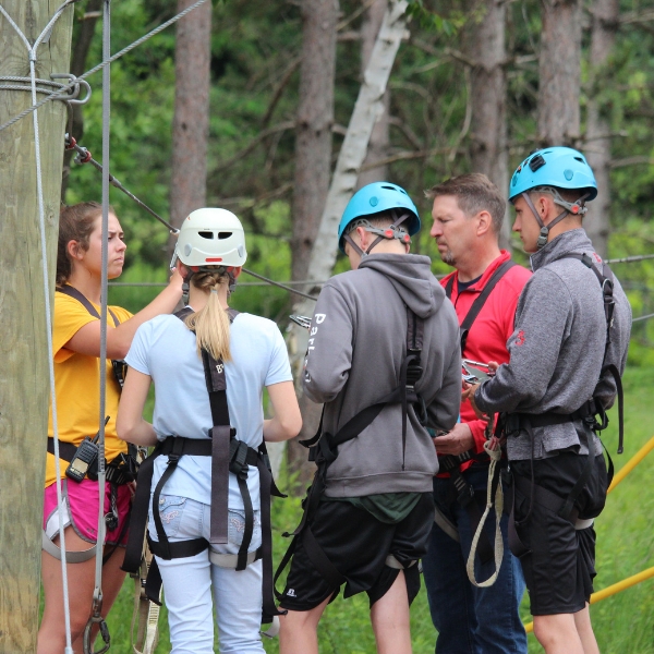 group of five people learning how to navigate the ropes course