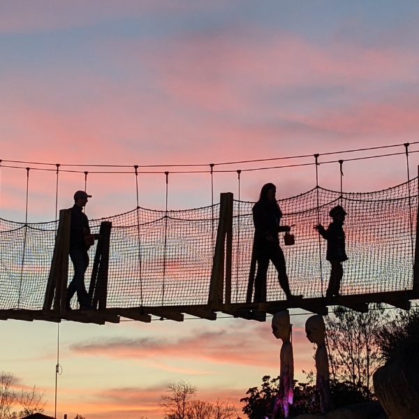 Three people walk on canopy tour bridge at twilight