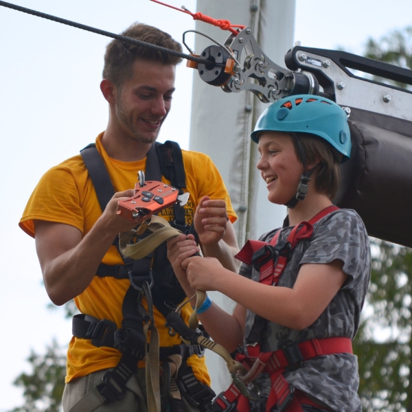 Smiling Adventure Guide helps girl with safety harness while standing on zipline platform