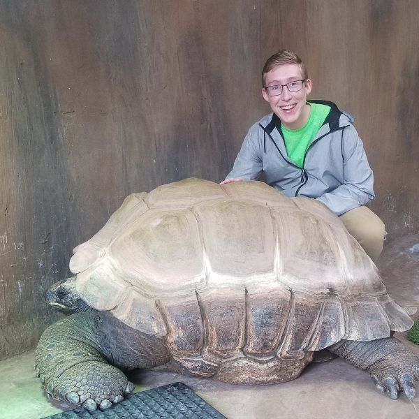 Smiling intern kneels behind giant Aldabra tortoise