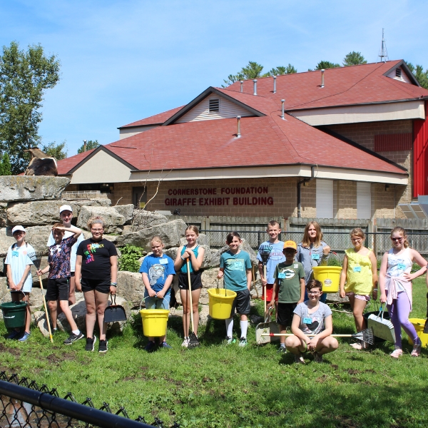 Smiling campers stand in goat yard holding rakes and buckets