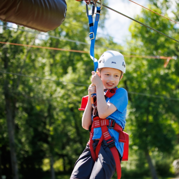 Smiling child hangs from harness on zipline