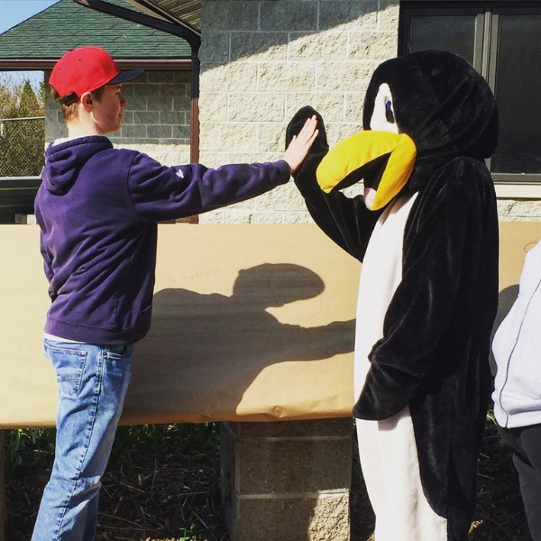 One teen volunteer gives high-five to volunteer dressed as penguin