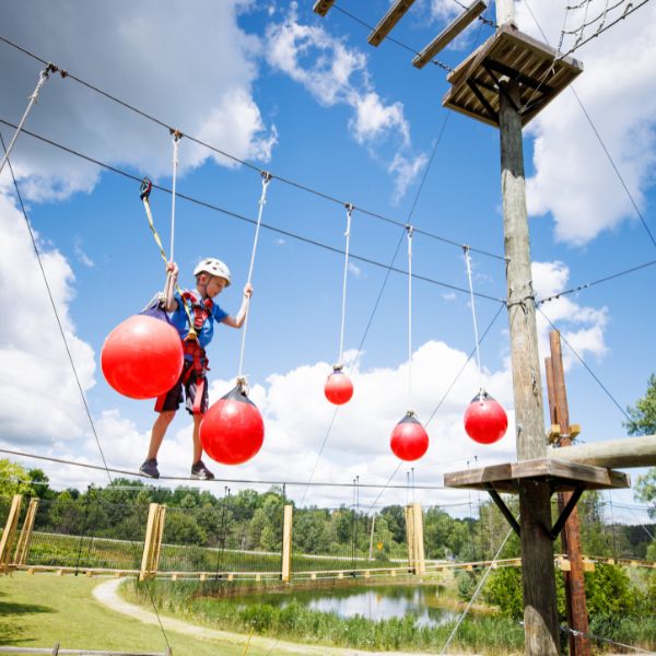 Boy balances on red balls high up on Ropes Course