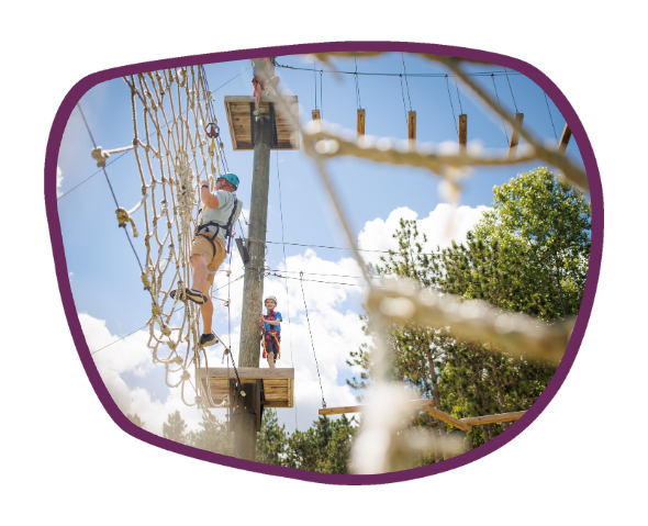 Viewed from below, a man in climbing gear hangs from web rope structure on the Ropes Course